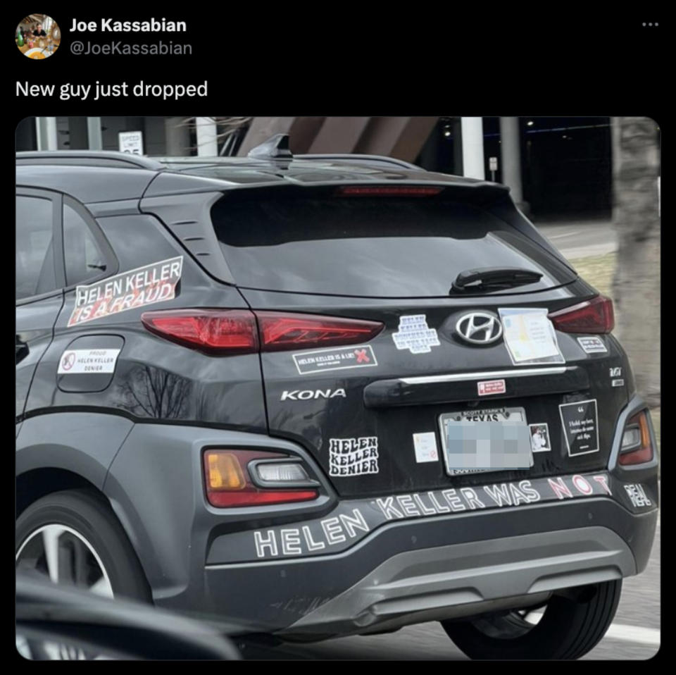 Car with multiple 'Helen Keller is a fraud' stickers, internet meme-centric decorations, in motion on the street