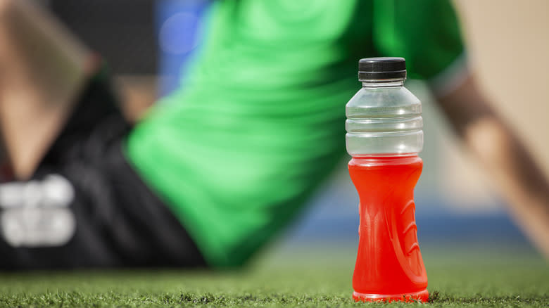 Red sports drink on turf with athlete sitting in background