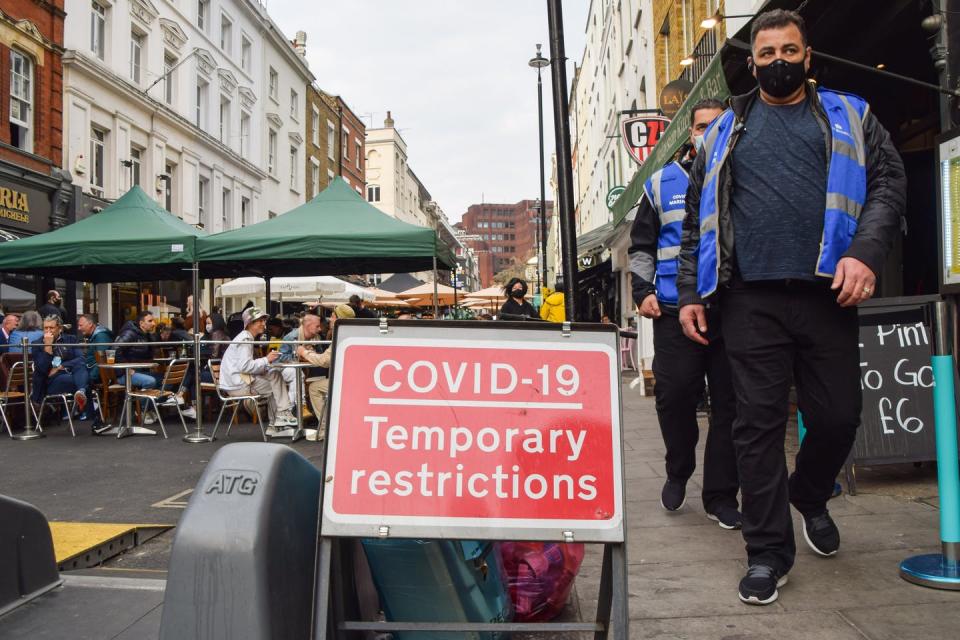 People walk past a COVID restrictions sign on a city street