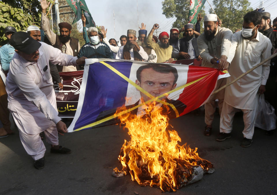 Supporters of Sunni Tehreek, a religious group, burn a representation of a French flag with a defaced image of French President Emmanuel Macron during a protest against the French president and republishing of caricatures of the Prophet Muhammad they deem blasphemous, in Lahore, Pakistan, Sunday, Nov. 1, 2020. (AP Photo/K.M. Chaudary)