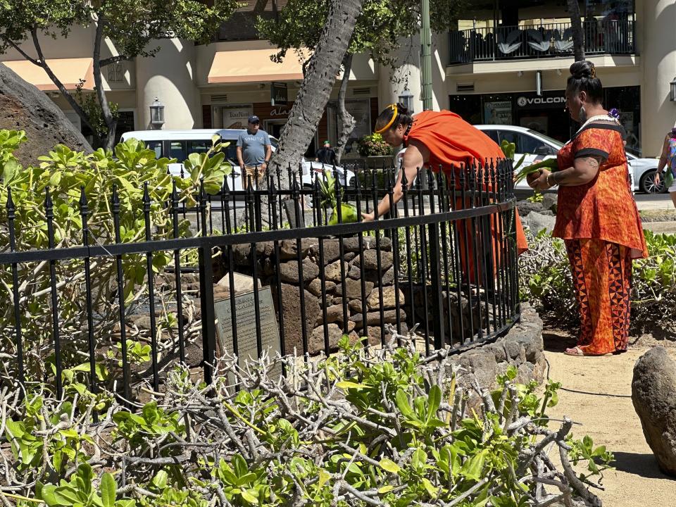 Charlani Kalama, left, a "kumu," or master teacher, assisted by Hinaleimoana Wong-Kalu, makes an offering at the Kapaemahu stones in Honolulu on Tuesday, Oct. 24, 2023 during a ceremony blessing a new plaque for the Waikiki monument. Honolulu officials introduced a new interpretive plaque for four large boulders in the center of Waikiki that honor Taihitian healers of dual male and female spirit who visited Oahu some 500 years ago. (AP Photo/Audrey McAvoy)