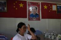 A woman adjusts her hair near a picture of paramount Chinese leader Mao Zedong surrounded by Chinese national flag at a community center in Pingtan in eastern China's Fujian province, Saturday, Aug. 6, 2022. Taiwan said Saturday that China's military drills appear to simulate an attack on the self-ruled island, after multiple Chinese warships and aircraft crossed the median line of the Taiwan Strait following U.S. House Speaker Nancy Pelosi's visit to Taipei that infuriated Beijing. (AP Photo/Ng Han Guan)