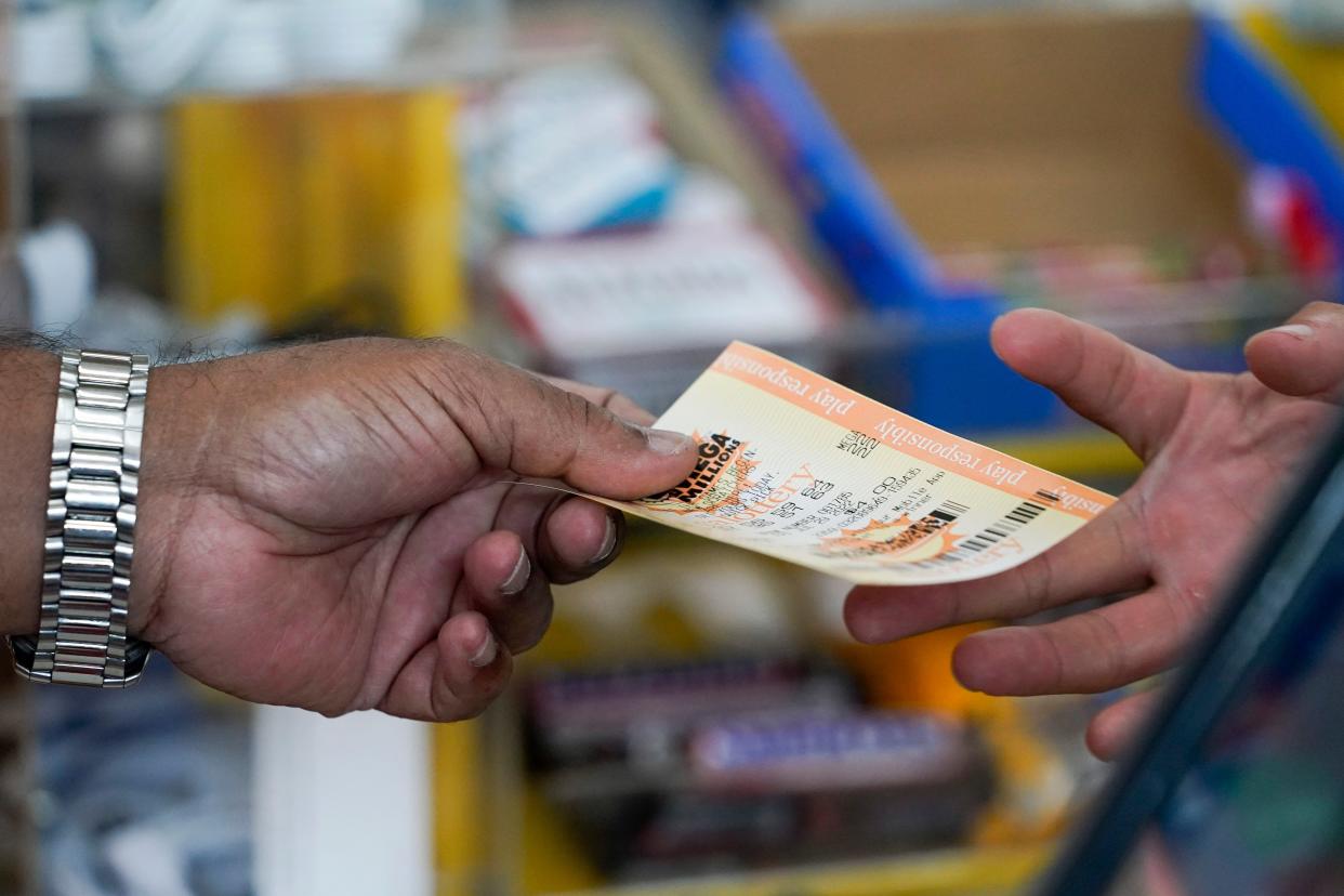 Ernie's Liquors owner Joseph Johny hands over a Mega Millions lottery ticket to a customer in Palo Alto, Calif., Friday, July 29, 2022. 