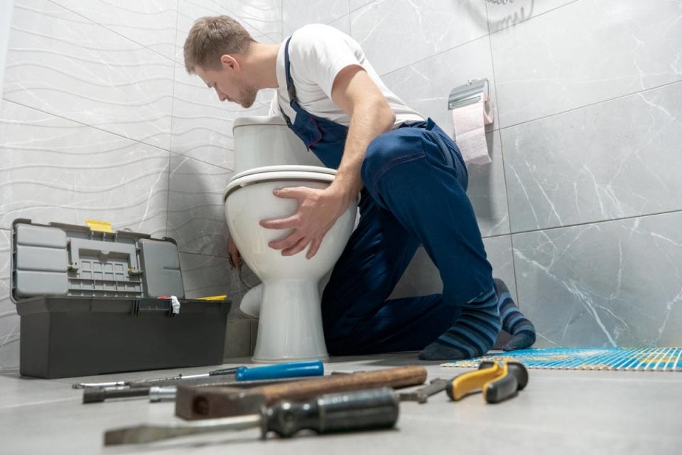 Professional installing new toilet with tools in foreground.