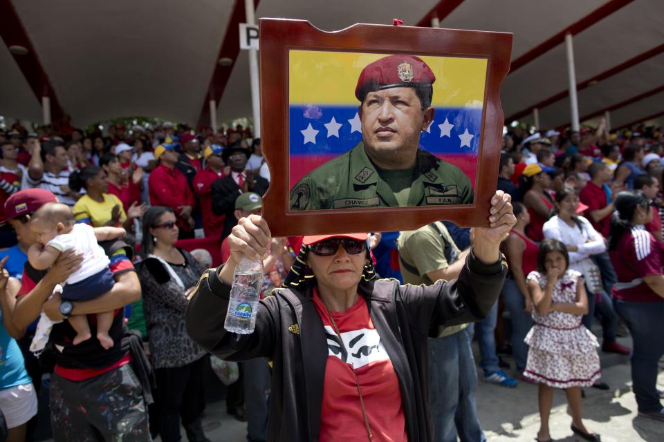 A woman holds up a portrait of Venezuela's former President Hugo Chavez during a military parade commemorating the one year anniversary of his death in Caracas, Venezuela, Wednesday, March 5, 2014. The anniversary of Chavez's death was marked with a mix of street protests and solemn commemorations that reflected deep divisions over the Venezuela he left behind. (AP Photo/Rodrigo Abd)