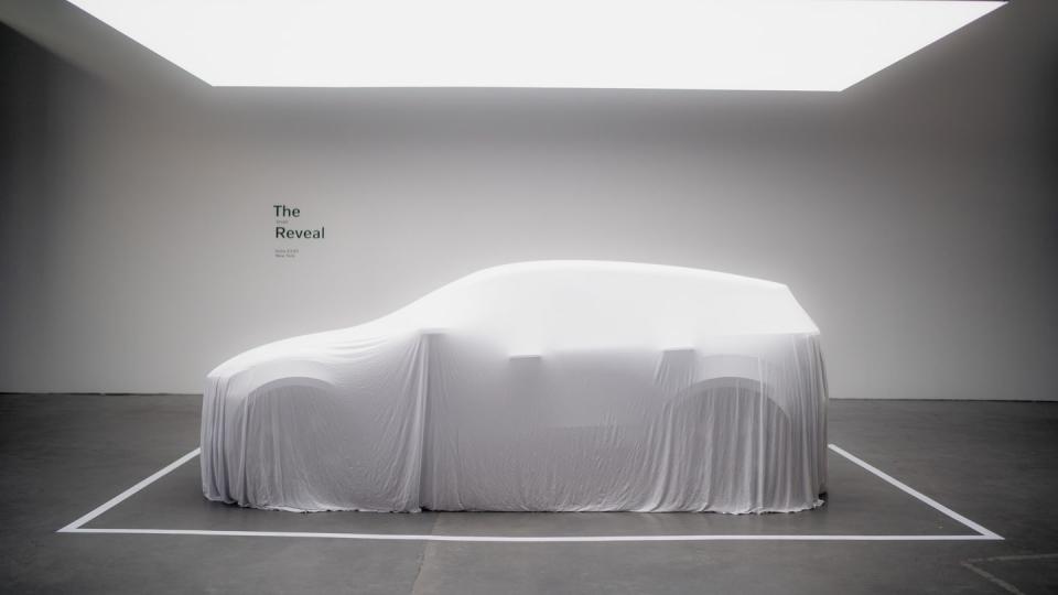 volvo ex30 crossover sits draped under a veil in a room with a light overhead
