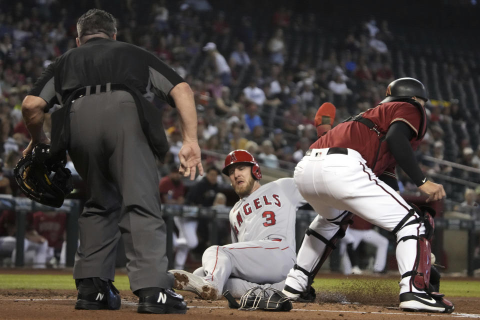 Los Angeles Angels' Taylor Ward (3) scores a run in between umpire Rob Drake and Arizona Diamondbacks catcher Carson Kelly in the second inning during a baseball game, Sunday, June 13, 2021, in Phoenix. (AP Photo/Rick Scuteri)