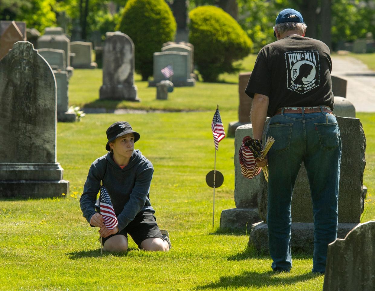 Declan Grenache, 15, decorates the graves of veterans for Memorial Day with his grandfather Harry Sechman at St. John's Cemetery Wednesday. Sechman, of Rutland, is a veteran of the U.S. Marine Corps and brought five of his six grandchildren to help the decoration effort. Volunteers from area veterans' groups, the Worcester County Sheriff's Office, and local businesses placed 5,000 American flags on graves in the cemetery.