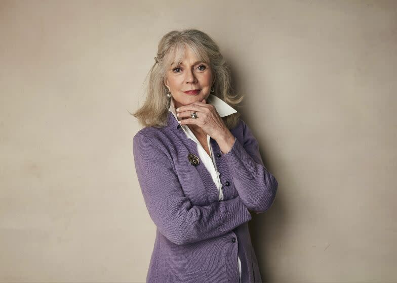 A woman with gray hair poses for a portrait with her chin resting on her hand