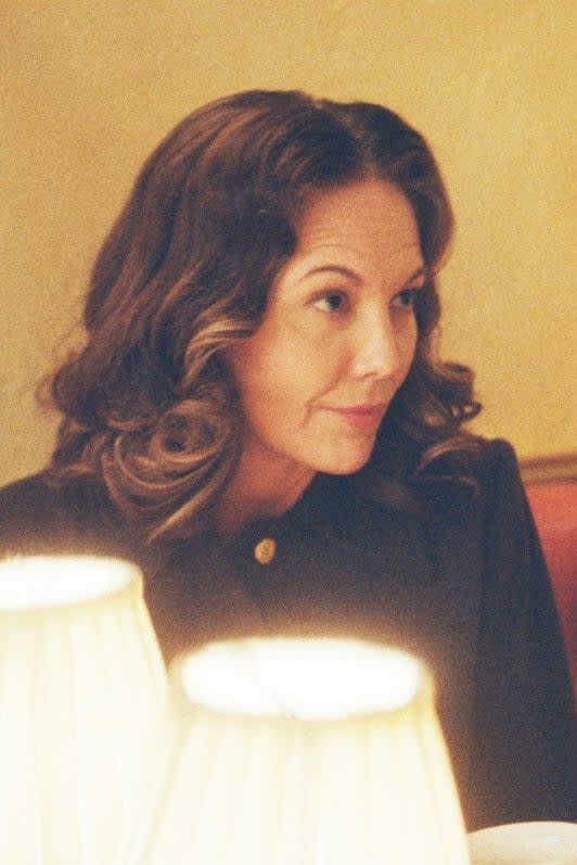 Diane Lane and Calista Flockhart sit at a restaurant booth, engaged in conversation, with wine bottles in the background