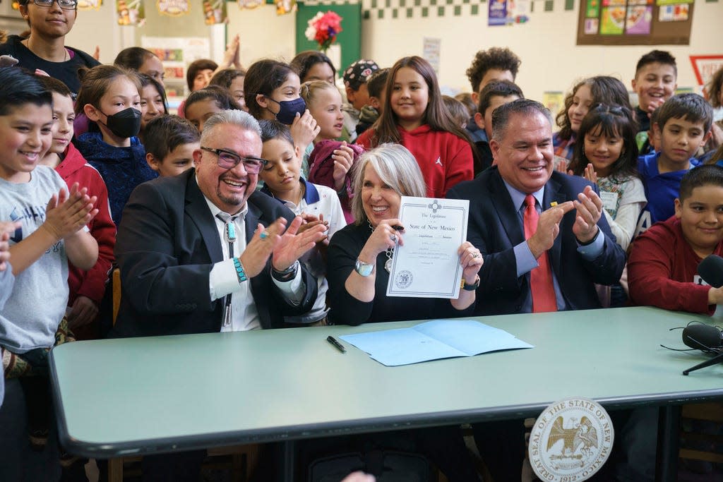 In this image provided by Gov. Michelle Lujan Grisham's office, the Democratic governor, center, holds a bill she signed during a celebration with sponsors Sens. Michael Padilla, right, and Leo Jaramillo, left, at Pinon Elementary School in Santa Fe, N.M., Monday, March 27, 2023. The legislation provides universal free school meals for New Mexico students.