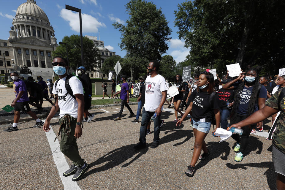 In this June 6, 2020, photo, Maisie Brown, 18, second from right, a member of the Mississippi branch of Black Lives Matter, leads a protest march past the Mississippi Capitol during a rally over police brutality, in Jackson, Miss. Young activists like Brown are energizing the debate about removing the Confederate battle emblem from the Mississippi state flag. Brown says elected officials must step up and change the flag. (AP Photo/Rogelio V. Solis)