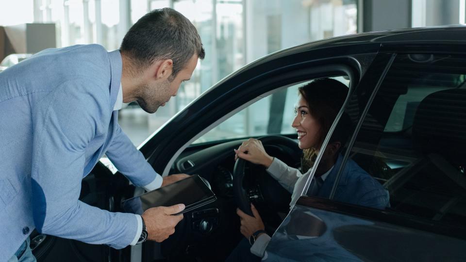 Vehicle dealer showing young woman new car.