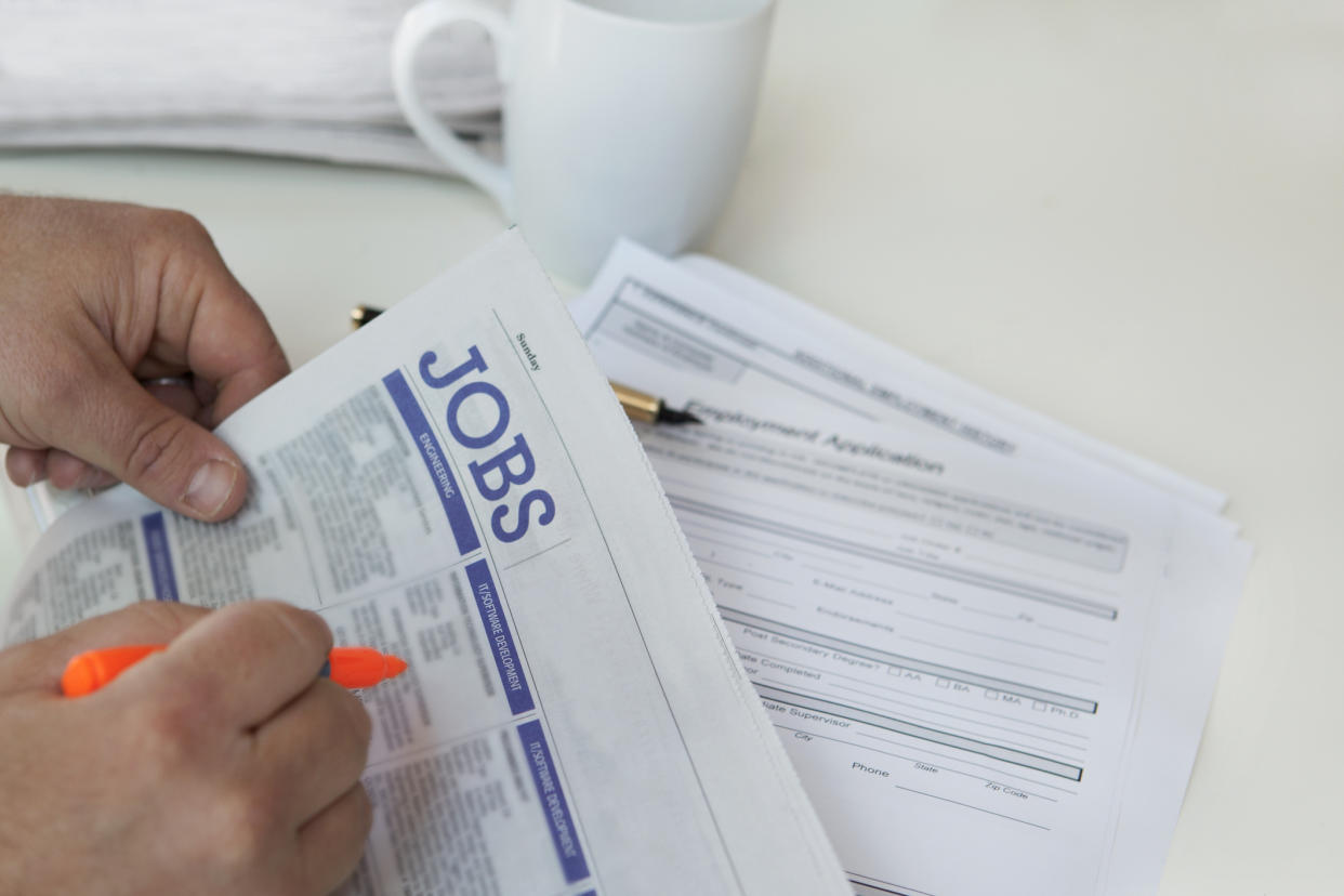 Close-up of hands finding jobs in newspaper with cup in background.