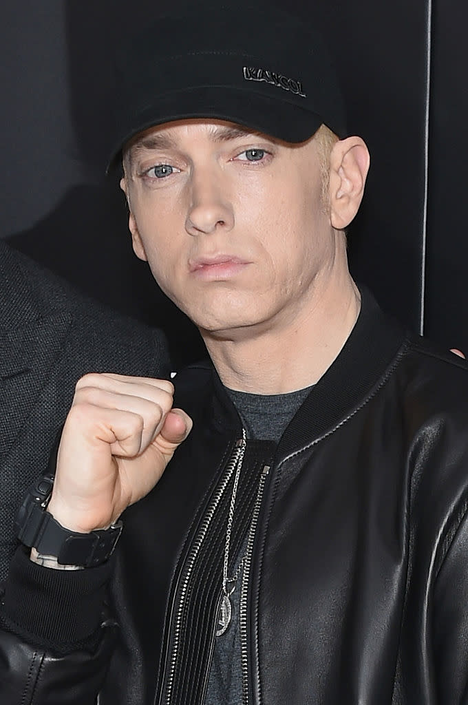 Eminem posing with a fist near his chin, wearing a baseball cap and black jacket