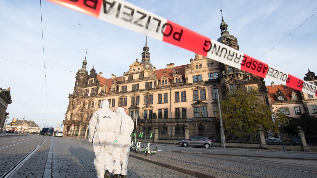 Zwei Mitarbeiter der Spurensicherung stehen vor dem Residenzschloss mit dem Grünen Gewölbe hinter einem Absperrband.