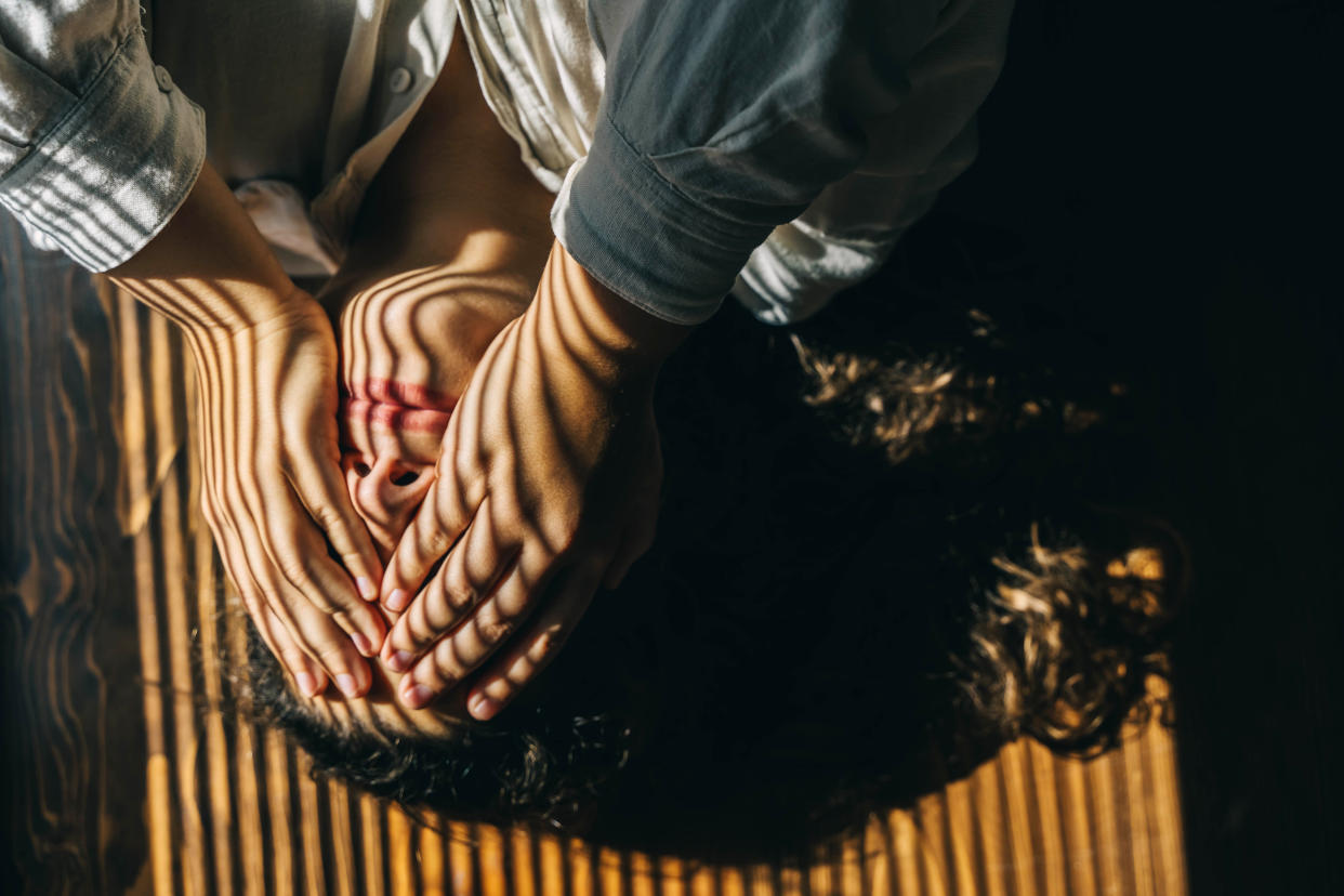 A woman lays on the floor in a shadow with her hands over her eyes and cheeks