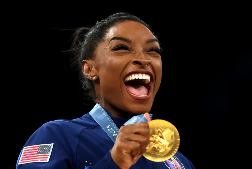 Simone Biles smiles as she holds her gold medal at the 2024 Summer Olympics in Paris.