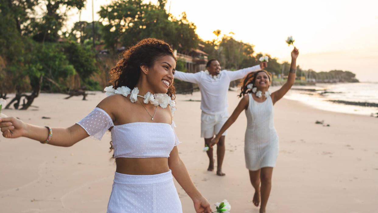 Happy friends celebrating reveillon on the beach, running and holding white flowers.