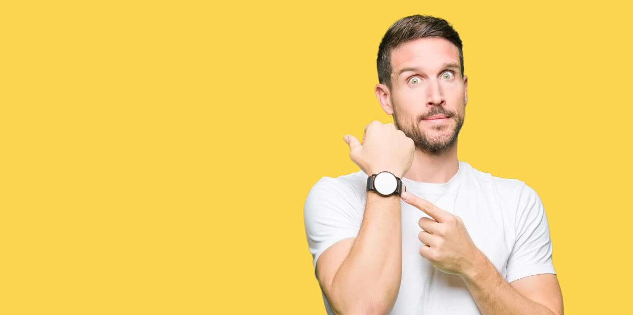 Handsome man wearing casual white t-shirt In hurry pointing to watch time, impatience, upset and angry for deadline delay