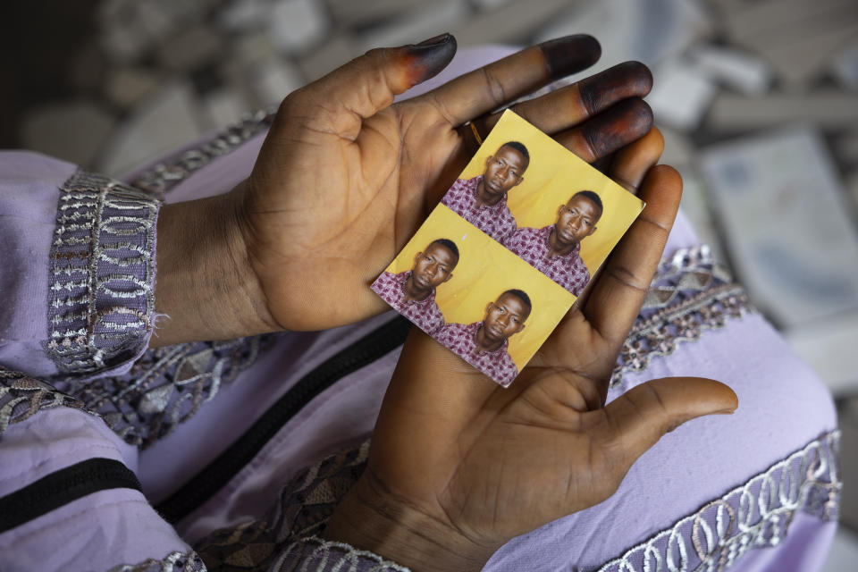 Mariama Sylla, sister of Ousmane Sylla, holds photos of him in their house at Matoto Bonagui, a suburb of Conakry, Guinea, Monday, April 8, 2024. Sylla had landed on Italian shores a year before his death in Feb. 4, 2024, one of tens of thousands of people who pay migrant smugglers hundreds or thousands of euros to cross the Mediterranean to reach Europe. He had no visa, and had been ordered to leave after admitting that he had lied about being a minor. (AP Photo/Misper Apawu)