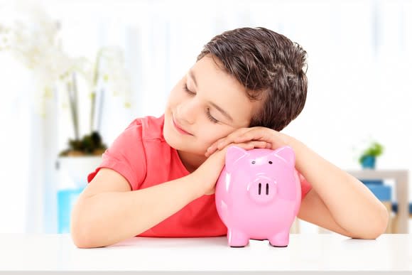 A child with his eyes closed rests his head on a piggy bank