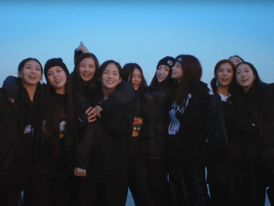10 girls dressed in black coats and sweatpants laughing and hugging each other on top of a roof