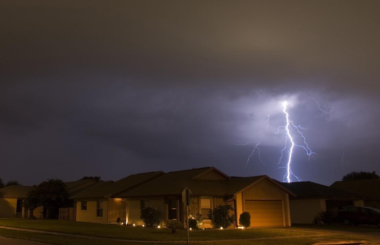 Houses with lightning striking in the night sky.