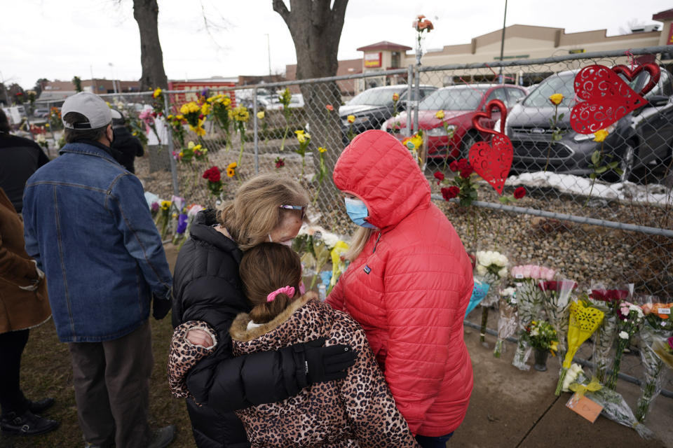 Mourners embrace after leaving bouquets on a fence put up around the parking lot where a mass shooting took place in a King Soopers grocery store Tuesday, March 23, 2021, in Boulder, Colo. (AP Photo/David Zalubowski)