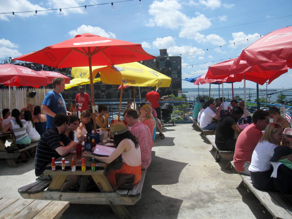 This July 6, 2013 photo shows diners at picnic tables with colorful umbrellas at Brooklyn Crab in Red Hook, a popular seafood eatery in a working-class industrial neighborhood in New York City's Brooklyn borough. The restaurant offers a view of the Brooklyn waterfront and is located across from old brick warehouses that now house a supermarket. Red Hook's restaurants and shopping have begun to attract a steady stream of New Yorkers and out-of-towners alike. (AP Photo/Beth J. Harpaz)
