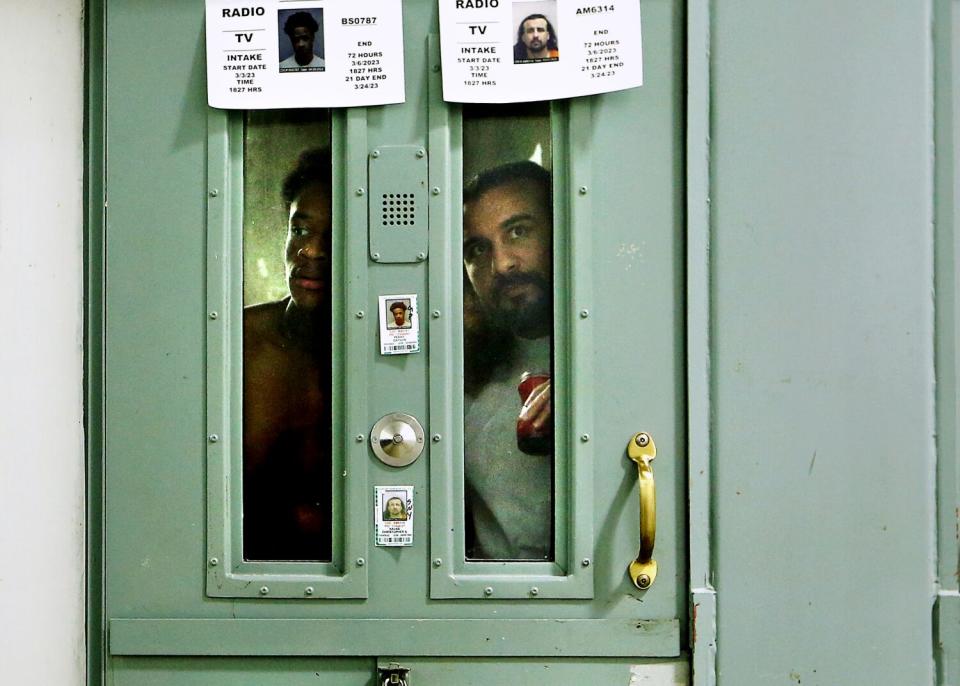 Two inmates looking through the narrow glass windows of a prison cell