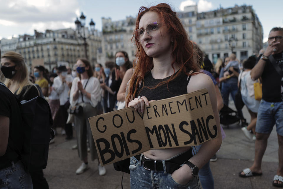 A woman holds a board reading '"Government Drink My Blood" as Women's rights activists protest against French President Emmanuel Macron's appointment of an interior minister who has been accused of rape and a justice minister who has criticized the #MeToo movement, in front of Paris city hall, in Paris, France, Friday, July 10, 2020. The French government said it remains committed to gender equality and defended the new ministers, stressing the presumption of innocence. Gerald Darmanin, Interior Minister, firmly denies the rape accusation, and an investigation is underway. New Justice Minister Eric Dupond-Moretti is a lawyer who has defended a government member accused of rape and sexual assault, and has ridiculed women speaking out thanks to the #MeToo movement. (AP Photo/Francois Mori)