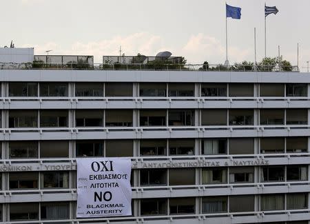 A Greek and an EU flags flutter atop the Finance Ministry as a banner is seen unfolded from a balcony of the building in Athens, Greece, July 1, 2015. REUTERS/Yannis Behrakis