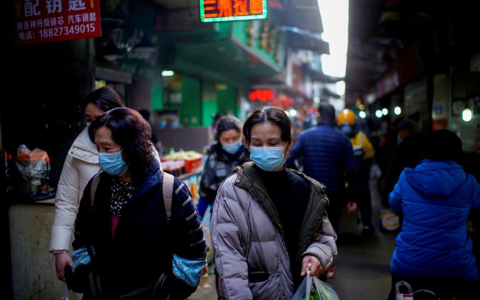 People wearing face masks walk on a street market in Wuhan - Aly Song/ REUTERS