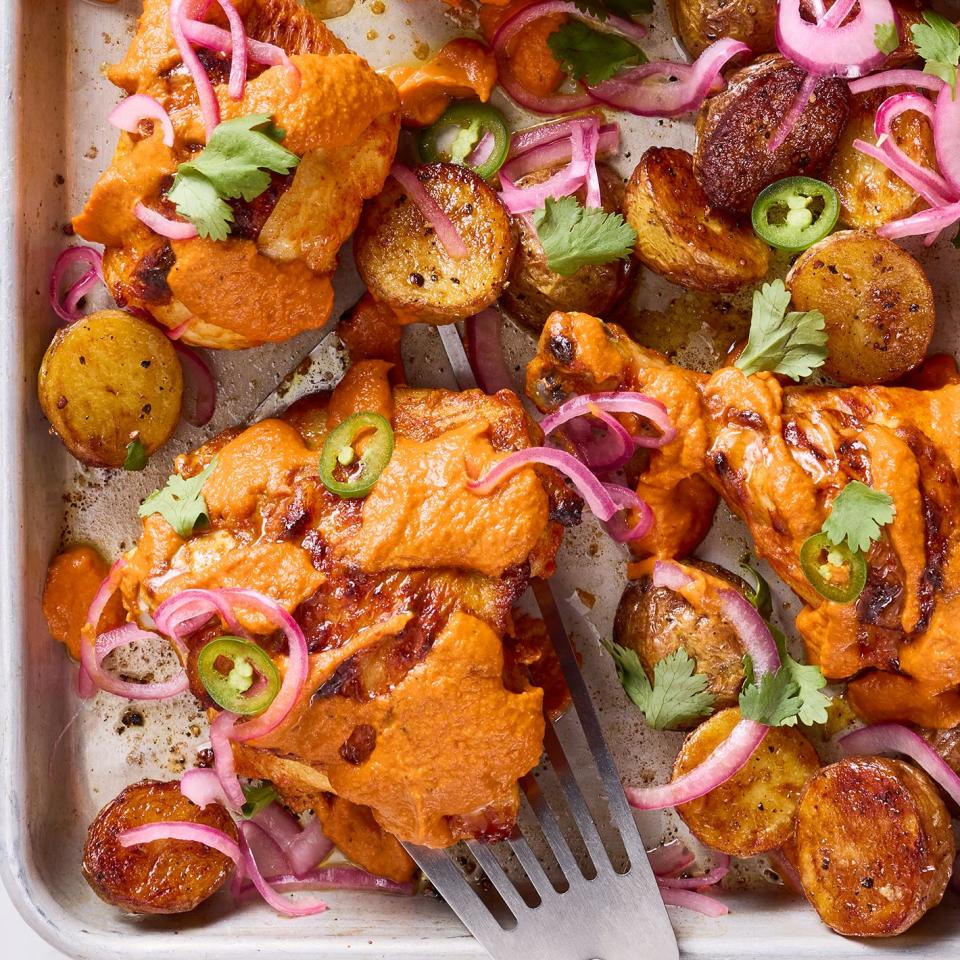 chicken thighs covered in a tikka masala sauce with pickled red onions and jalapenos on a sheet pan