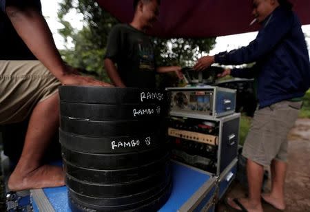 Workers stand next to cans containing copies of the film 'Rambo', before a wedding party in Bogor, Indonesia, February 18, 2017. REUTERS/Beawiharta/Files
