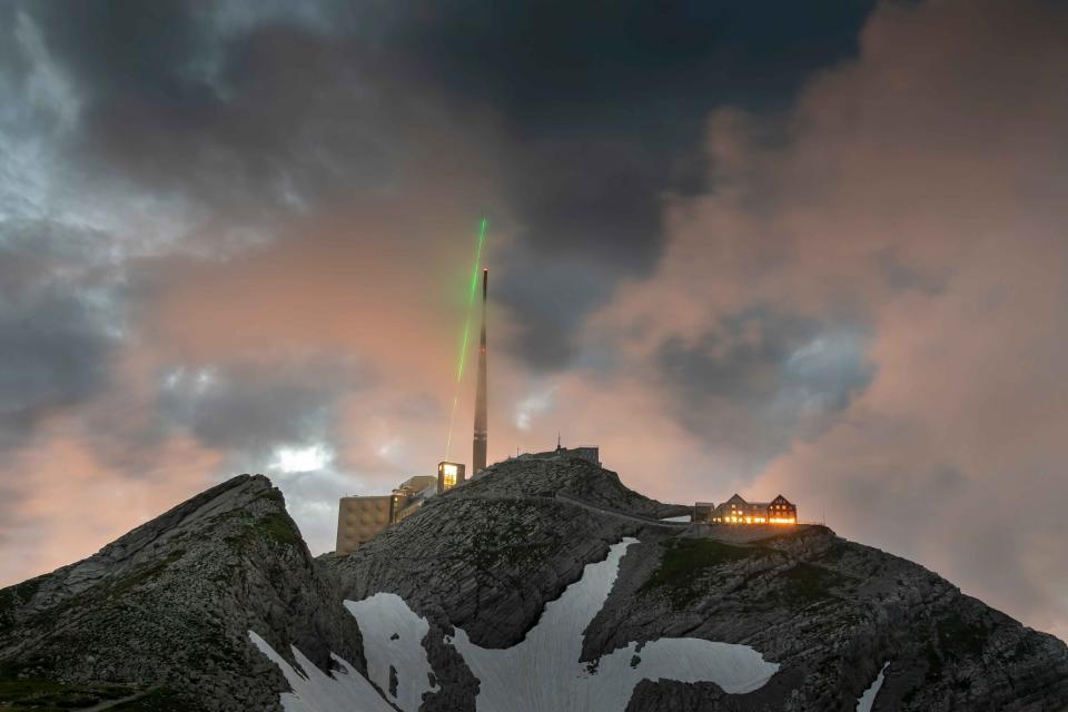 The Laser Lightning Rod is shown shooting into the sky on top of a swiss peak covered with snow