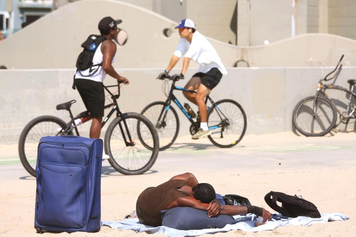 A homeless person sleeps on belongings on the beach a couple of blocks