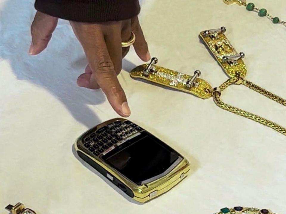 hand pointing to golden Blackberry and jewelry to be auctioned off by Pharrell Williams