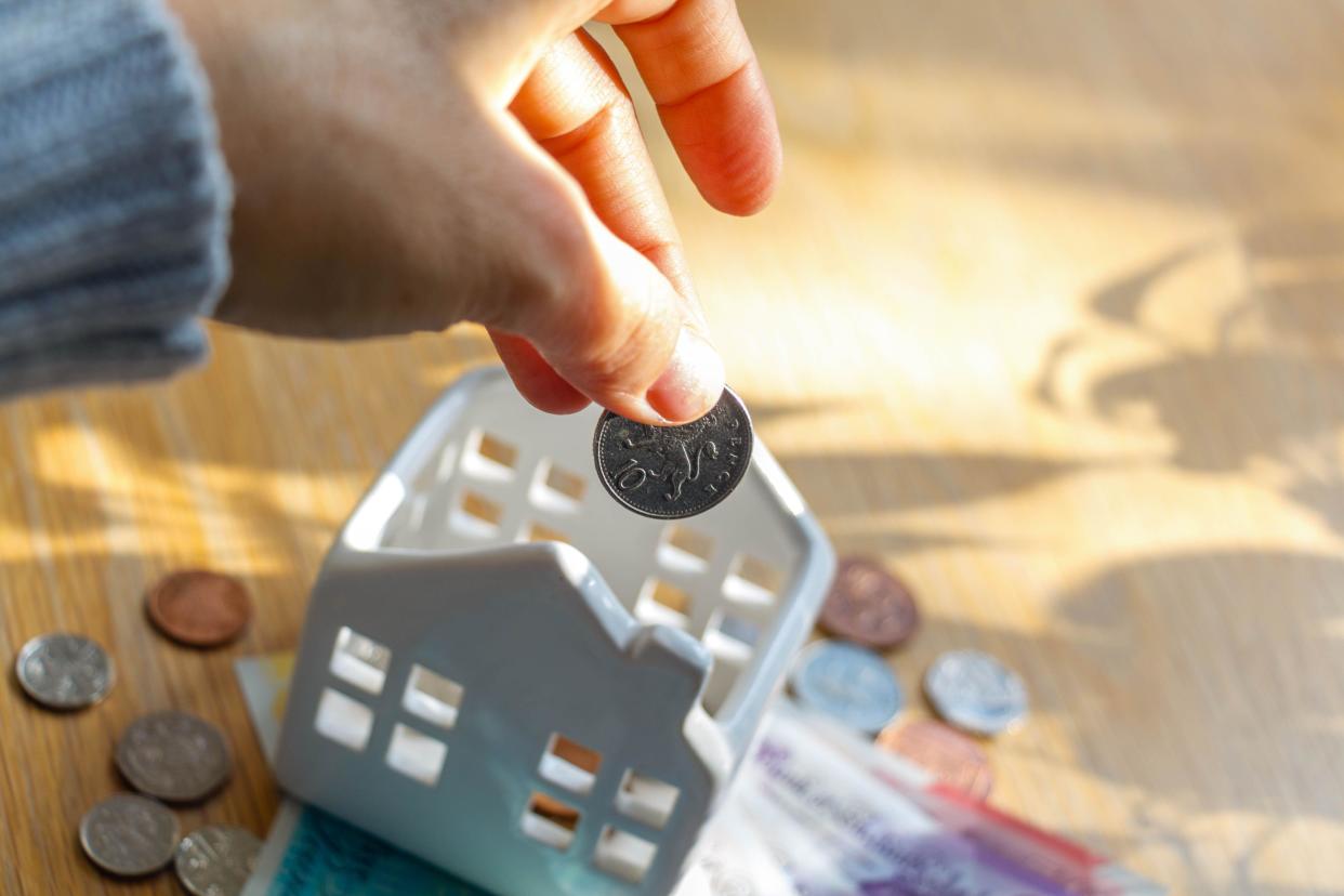 Close-up of a hand putting a coin in ceramic house piggy bank