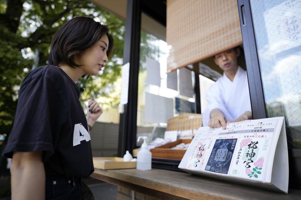 Momo Nomura, left, chooses a design of Goshuin, a seal stamp certifying her visit that comes with elegant calligraphy and the season’s drawings, at Sakura Jingu shrine in Tokyo on Aug. 30, 2023. Nomura says she enjoys the stamp designs, and shrine visits allow a moment of reflection and a change of pace from her busy life as a graphic designer and entrepreneur. (AP Photo/Eugene Hoshiko)