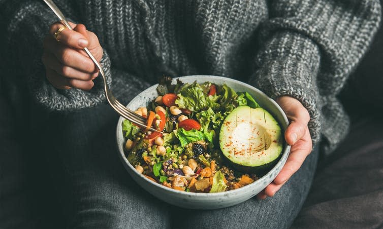 A woman holds a bowl of vegetarian foods.