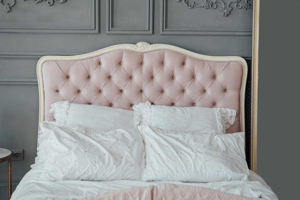 Large buttoned headboard of luxury bed, beige and pink pillows on it, copy space. Feminine bedroom in pink and white colors. Chesterfield style checkered soft headboard, diamond pattern