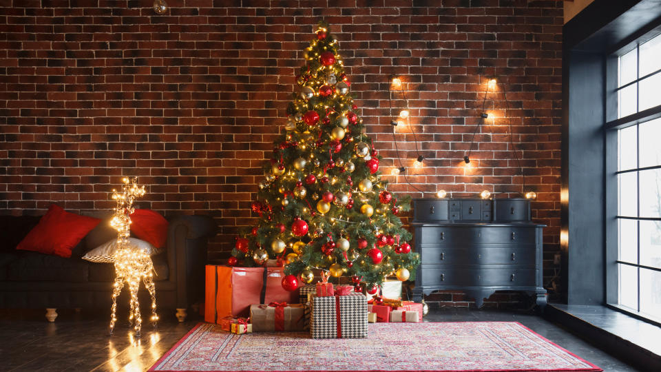 Christmas, New Year interior with red brick wall background, decorated fir tree with garlands and balls, dark drawer and deer figure