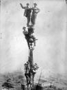 <p>Construction workmen cling to chains as they dangle in mid-air off the side of a skyscraper.</p>