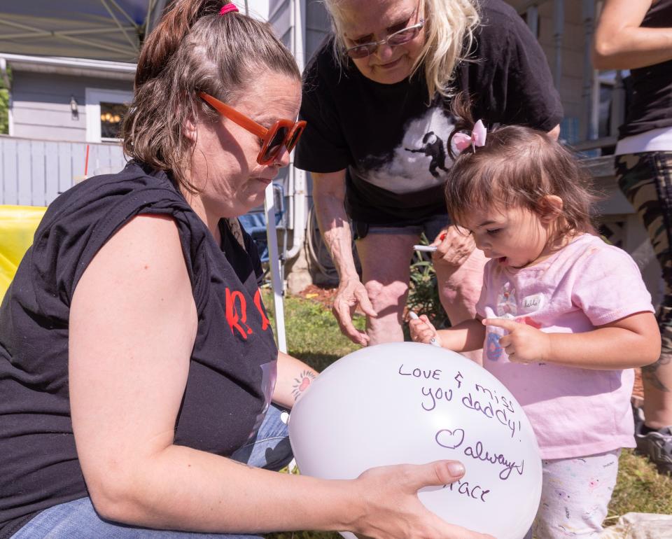 Zachary Fornash's daughter, Gracie, 1, draws on a balloon for her father with the help of her great-aunt Dora Lee Dennis, left, and Julie Vlach, her great-grandmother, prior to a balloon launch in Fornash's memory. Fornash was shot and killed by a Canton police officer on Dec. 5, 2023. He would have turned 25 on July 18.