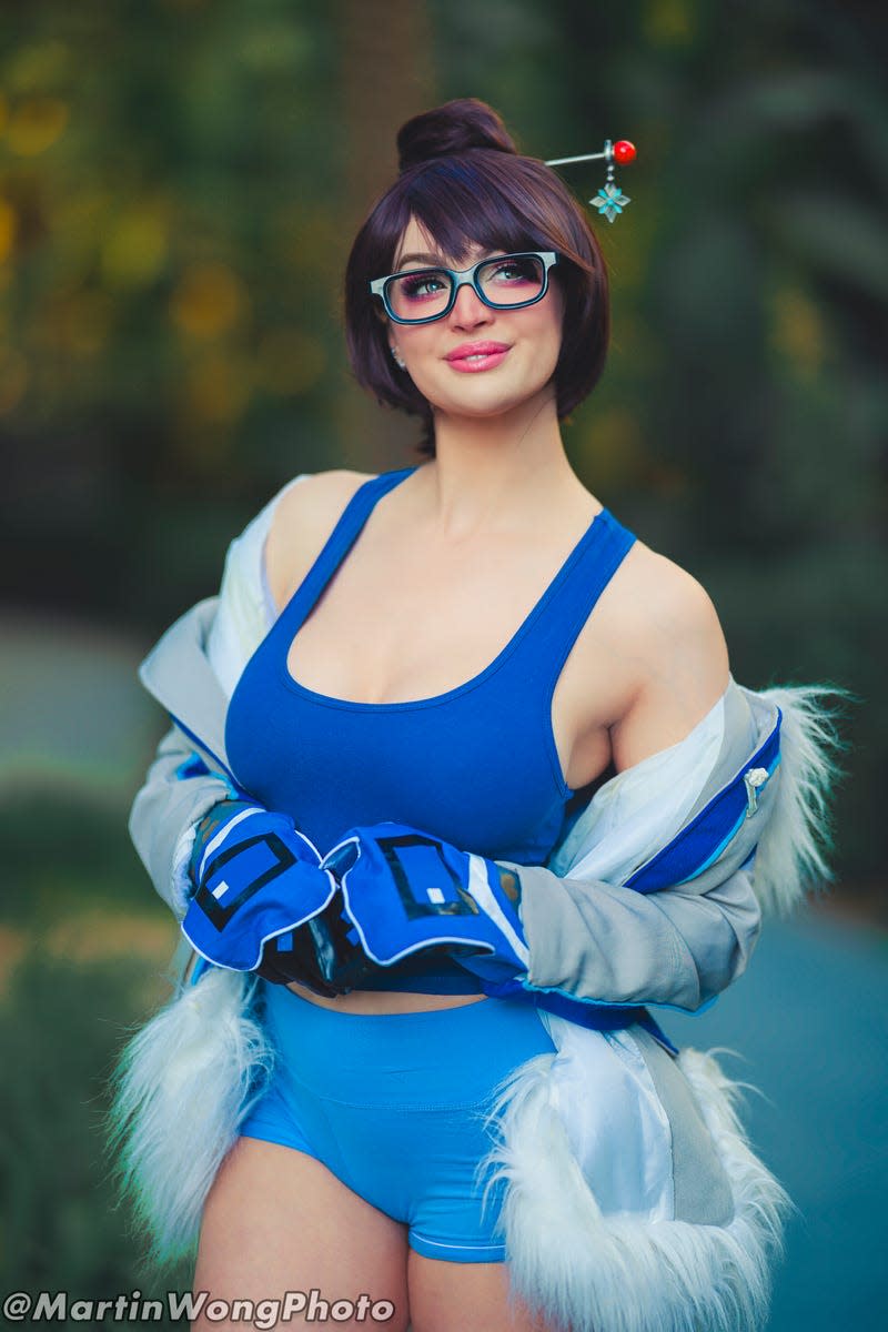 A Mei cosplayer looks off camera and smiles. 