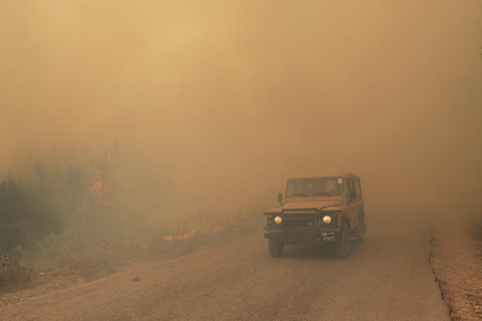 A Lebanese army vehicle drives past flames of a forest fire, at Qobayat village, in the northern Akkar province, Lebanon, Thursday, July 29, 2021. Lebanese firefighters are struggling for the second day to contain wildfires in the country's north that have spread across the border into Syria, civil defense officials in both countries said Thursday. (AP Photo/Hussein Malla)