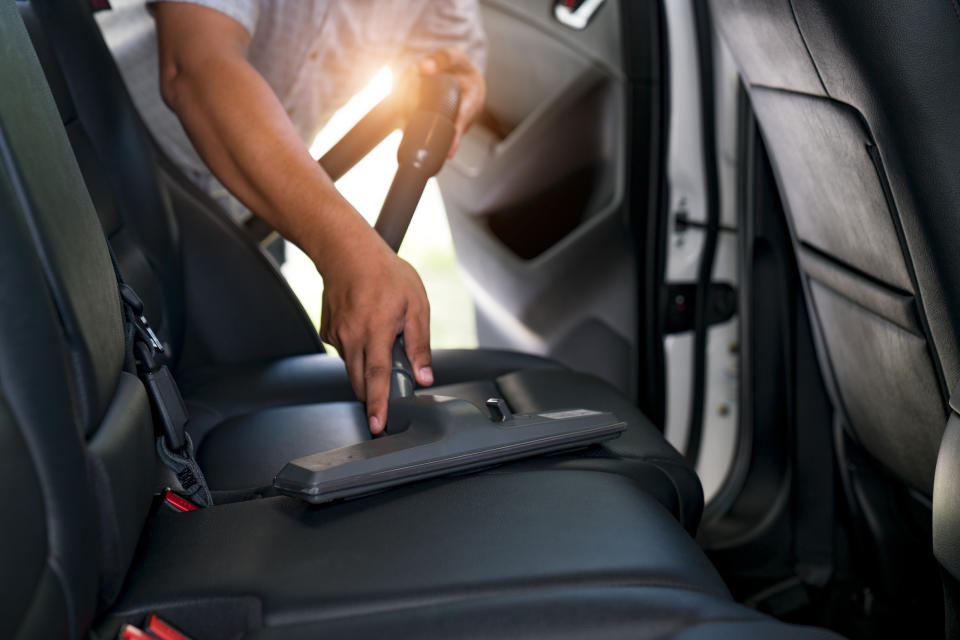 A person using a vacuum cleaner to clean the back seat of a car