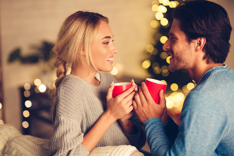 Couple in love drinking tea and enjoying winter holidays in front of Christmas tree